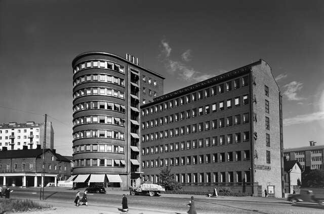 mustavalkokuva tiilisestä kerrostalosta, jossa on kaareva tornimainen osa