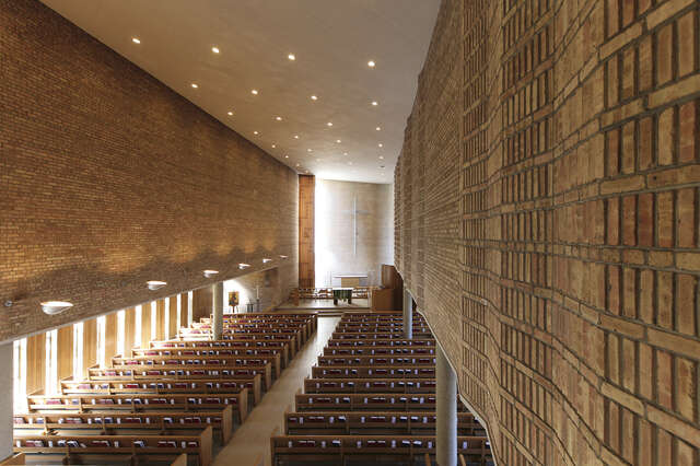 Interior of a church hall with an undulating yellow brick wall.