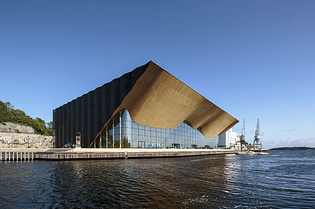 A building with a wavy wooden canopy by the water