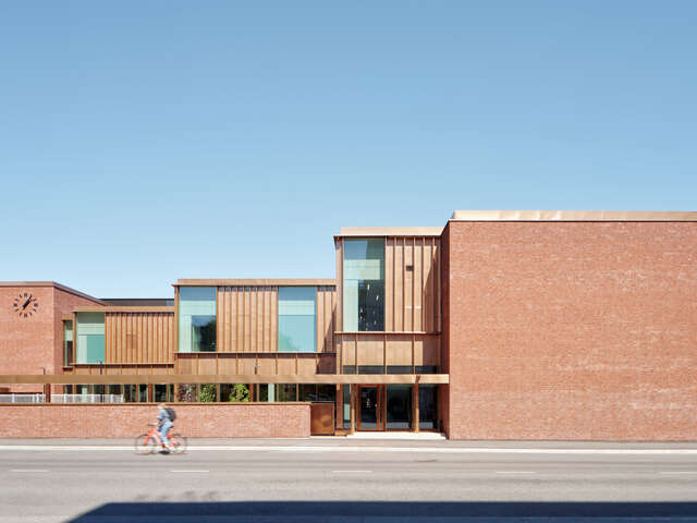 A geometrical red-brick building set back from the street in stepped volumes, creating an enclosed courtyard.