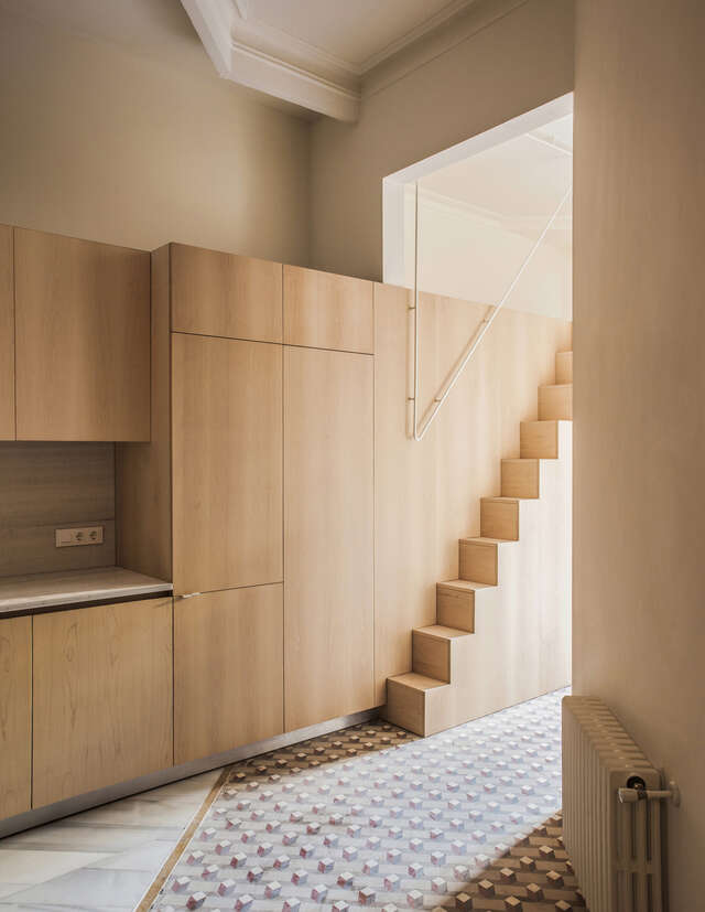 A kitchenette with wooden cabinet doors and very narrow and steep wooden stairs
