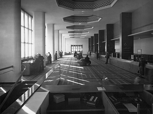 Interior of the main hall with pilasters and windows on the left side, service desks on the right side. Ceiling details and lounge spots in the middle.