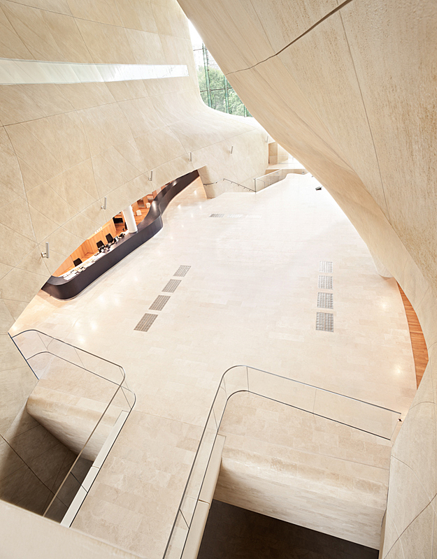Entrance hall made of light beige stone and a walkway with glass railings