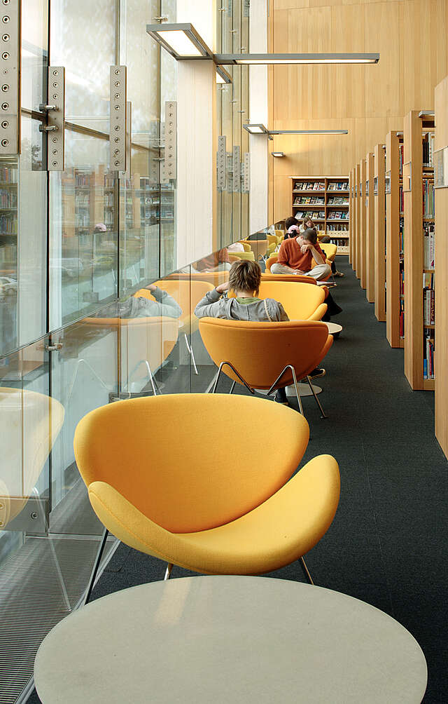 Yellow armchairs between bookshelves and glass wall.