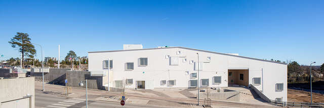 White facade of a multiple storey building with a white facade, square windows seemingly distributed without a pattern and a gable roof.