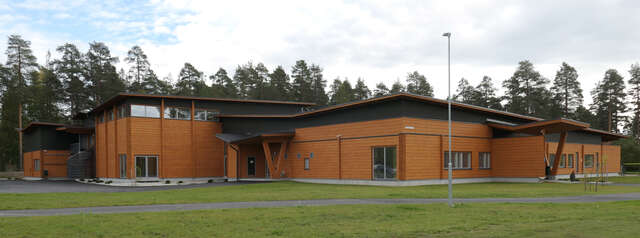 Massive oblique wood columns and beams and free-form angularity of the low-pitched roof characterize the exterior of the building as well as a contrast between orange-coloured structures and dark walls.
