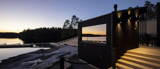 Small dark wooden hut in the foreground with water and pier to the left.