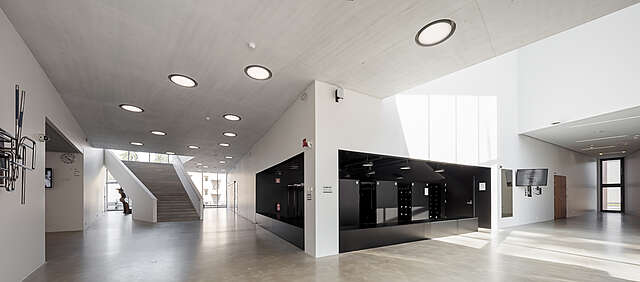 Modern lobby with white walls, concrete floors, large windows and a black wardrobe.