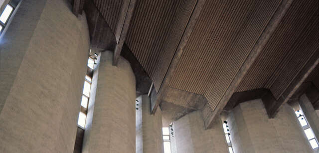 Church interior with concrete walls and ceiling with wooden beams covering most of the concrete.