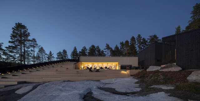 front of the building's exterior. Rocks in the foreground and a forest behind the structure.