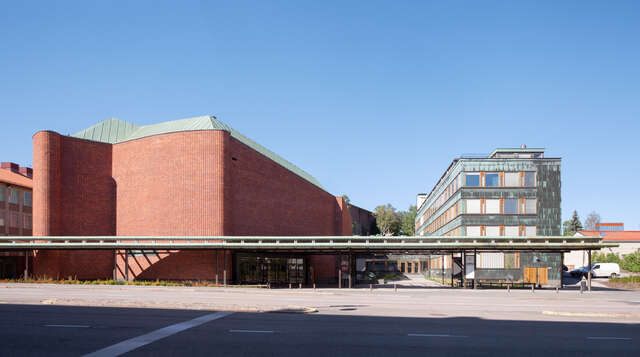 Red brick building with a lower connecting part to copper-clad office. In the foreground a canopy throughout the building complex