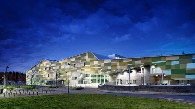 Different-sized cement composite panels in white and shades of green are used to create a vivid and playful patchwork. The facades are punctuated by protruding aluminium-framed windows.