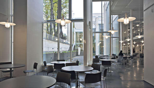 White interior with black round tables and chairs, hanging light fixtures and window walls ahowing the yard.