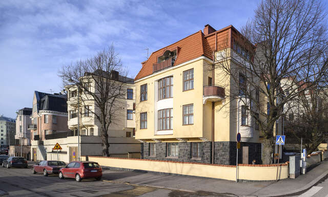 Yellow villa with brown window frames and balcony and a stone base.