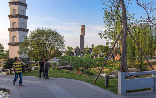 Tower of a sculptural church rising up in the horizon of a park, a couple of visitors in the foreground
