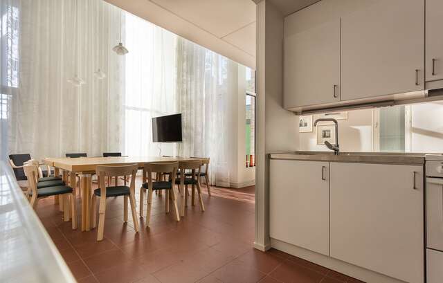 White kitchen with large table and 12 chairs to the left on a red rile floor.