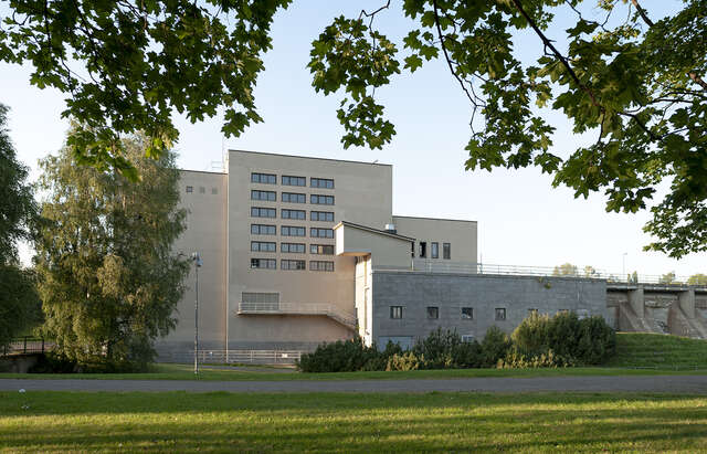 Photo showing grass aea in front of the power plant, as well as the facade of the powerplant, that from this point of view is divided in three main masses.