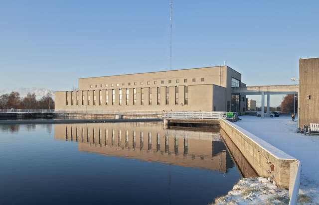 Photo of the horizontal facade of the powerplant over the river, smooth as glass in this picture.