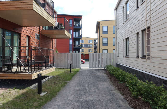 Pedestrian street between new, yellow and red 4-storey high blocks of flats and an older, white wooden house.