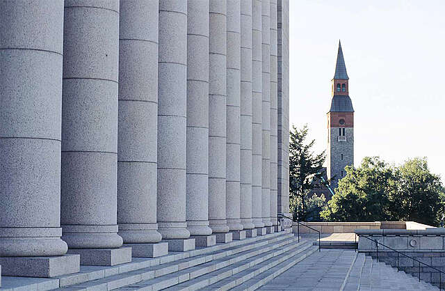 Side view of the massive granite columns of the Parliament House with a tower in the background.