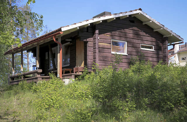 Picture of a log-built dark wooden residential cottage in the summer.