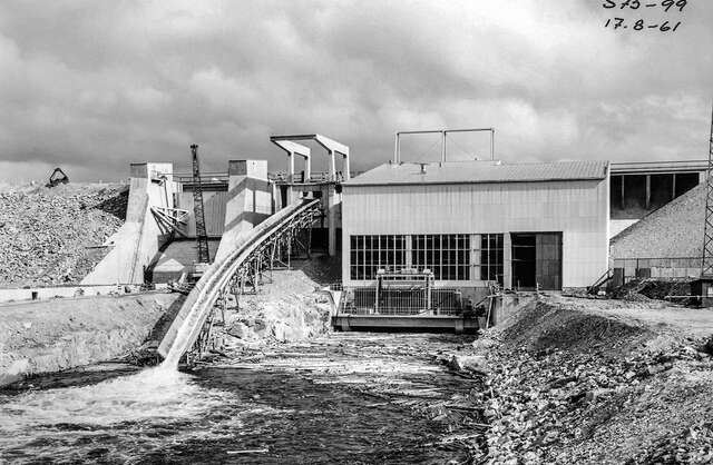Black and white photo of the hydropower plant in use, water flowing through the structures back into the river.