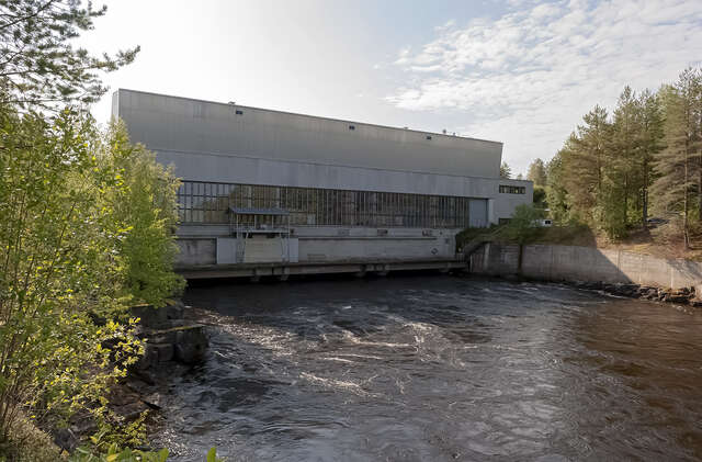 View over the river towards the hydropower plant with pitched roof and rectangular, vertical windows.