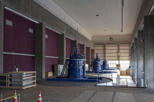 Machine hall including bright blue machinery and deep purple-colored wall in the background. Natural light flows into the space beautifully from between the concrete structure.