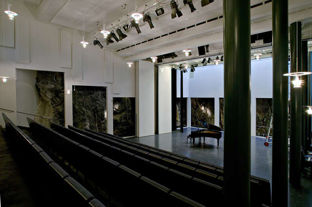 Auditorium with a grand piano on stage, the rock formation is visible through the walls.