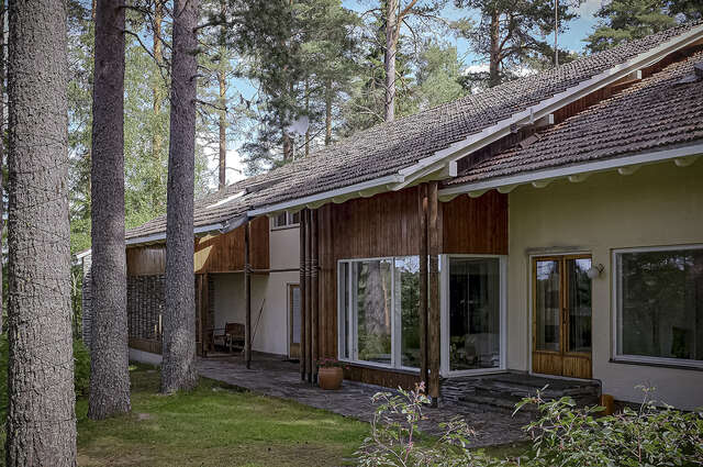 Photo of the terraced house showing how the eaves of the tile roof reach over the outer walls, creating a stron architectural element. The façade is divided into sections by changing the material at times from wood to white plaster.