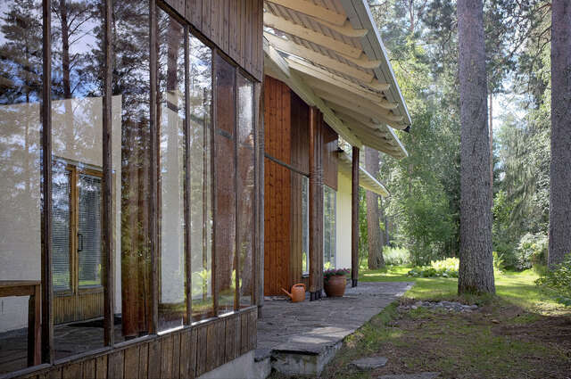 Photo of the terraced house showing how the eaves of the tile roof reach over the outer walls, creating a strong architectural element. The façade is divided into sections by changing the material at times from wood to white plaster.