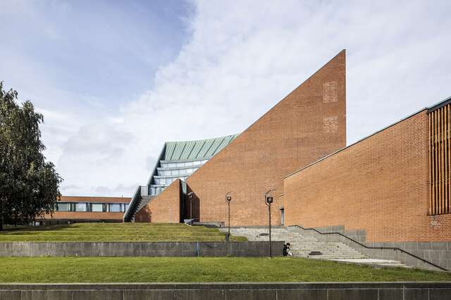 Red-brick building with triangular wall, tiered windows and a green copper roof.