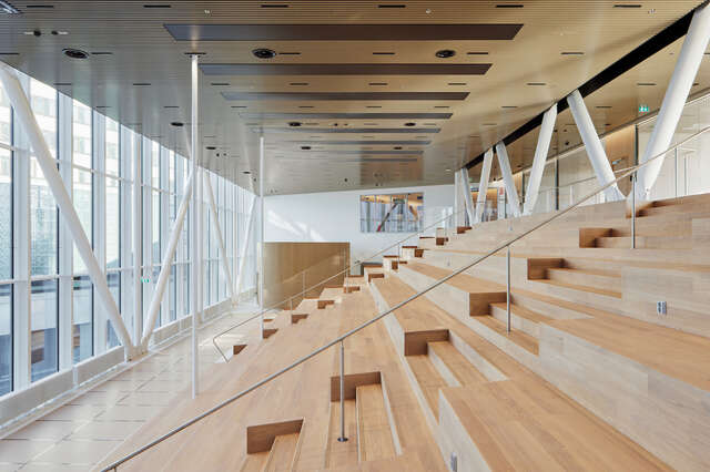 A large room with a wooden rising seating area, with natural light.