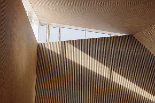 A small, triangle shaped window in the corner of a wooden wall and ceiling.