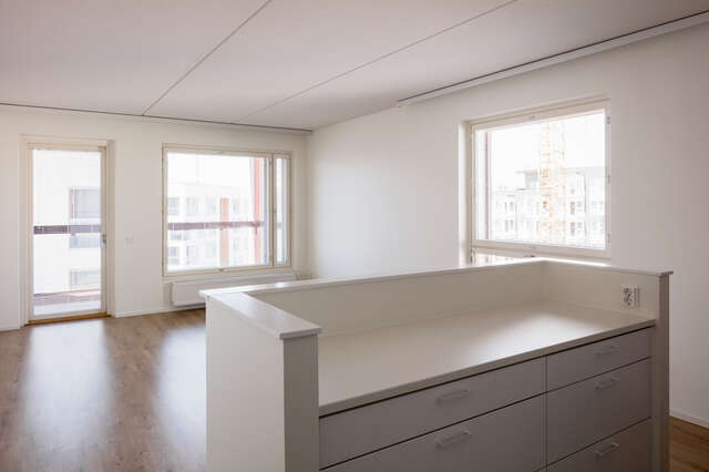 An empty room inside an apartment building. White walls and a wooden floor can be seen.