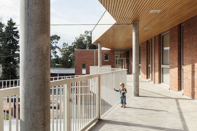 A small child leaning on a metal fence of a large brick building