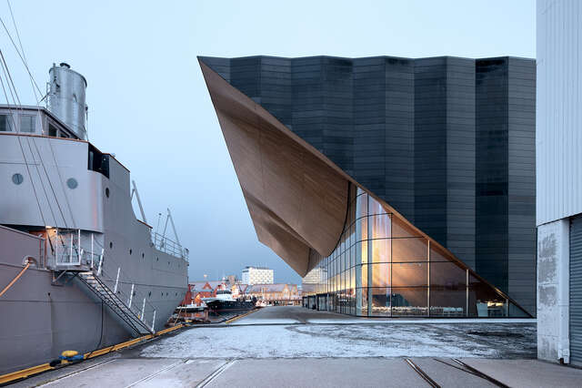 On left a ship, right next to it a dark, triangular side facade and a wavy wooden canopy