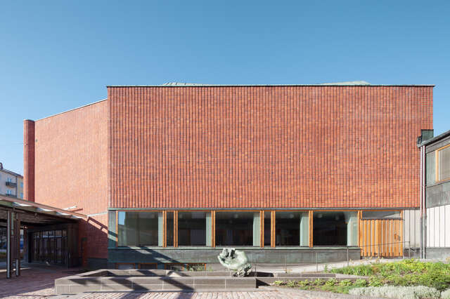 In a piazza monolithic exterior displaying bent red brick surfaces and a line of windows