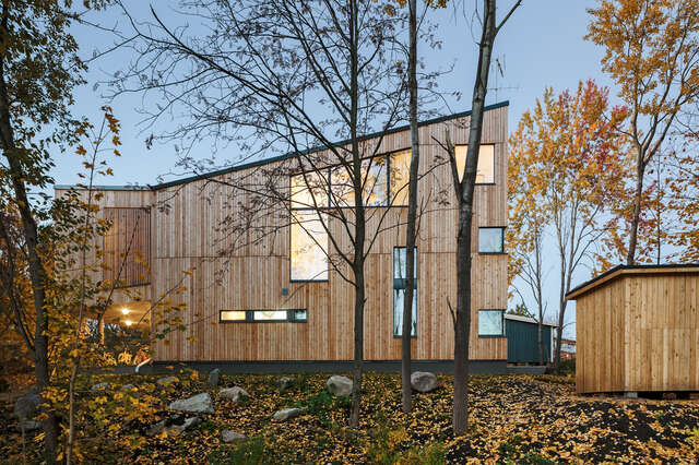 House with wooden façade, diagonal roof and multiple windows, small wooden building on the right