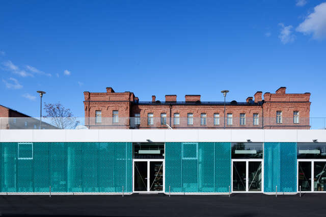 Turquoise-white-transparent façade in front of red brick barrack