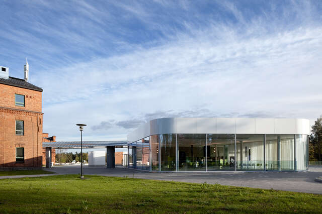 White and transparent annex with rounded angles, steel canopy and red brick barrack