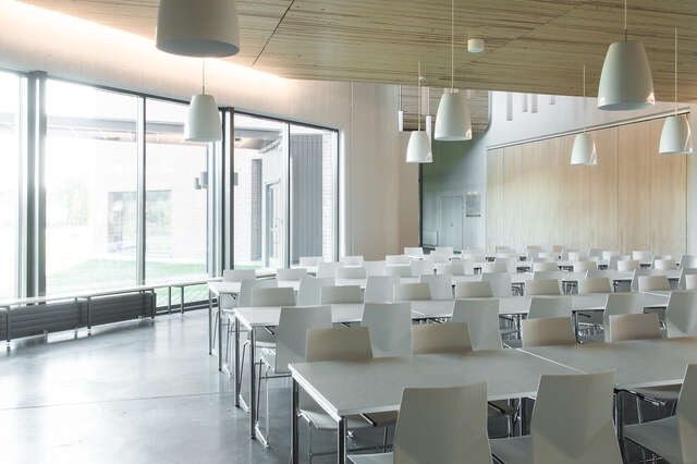 Light space with white sitting areas and hanging lights, wooden ceiling and large windows