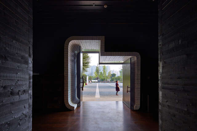 View from the dark church inside through open doors to a yard picturing a girl in a dress, trees and city silhouette in the background