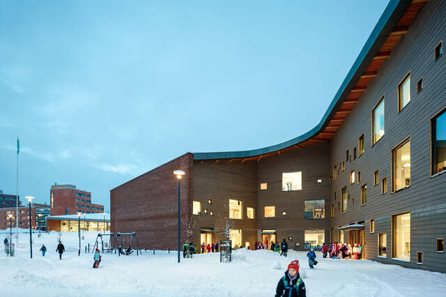 Brown-coloured façade with multiple square windows, children playing in snowy school yard