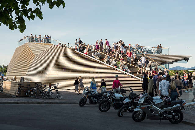 Wood panel facade with a crowd of people on the terrace.