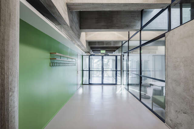 Hallway with a wardrobe on a green wall, large window walls and visible concrete structures.