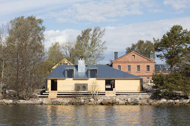 Wooden sauna with a dark roof on the shore.