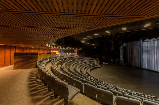 Theatre seats in a semi circle around the stage, the wooden ceiling and walls give the room a warm feeling.