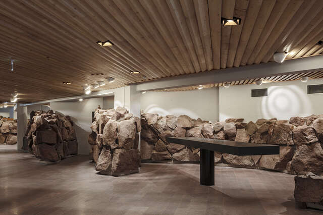 Meeting area with a standing tables, Boulder covered white walls and a wooden ceiling.