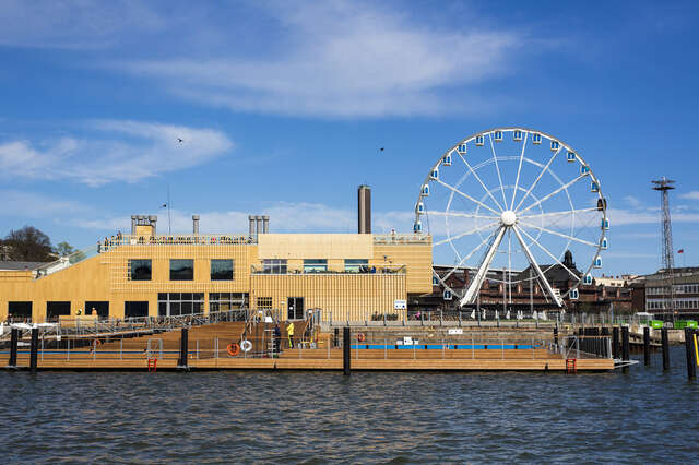 Wooden facade of the Allas sea pool with a Ferris wheel in the background.